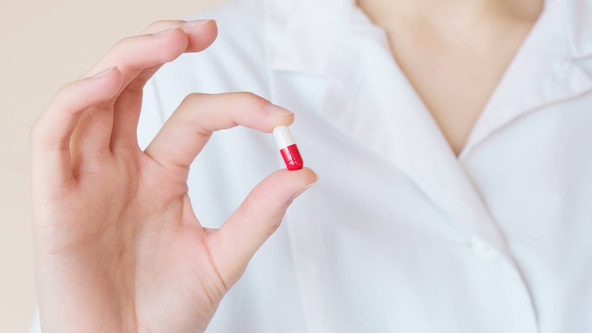 Woman in a doctors coat holding a single pill