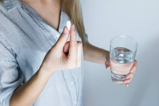 Woman holding a pill and a glass of water.
